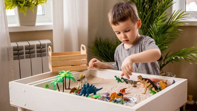 boy playing sensory box dinosaur world kinetic sand table