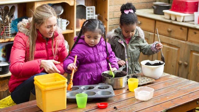 Two children outdoors using a big mental pan to make mud pies