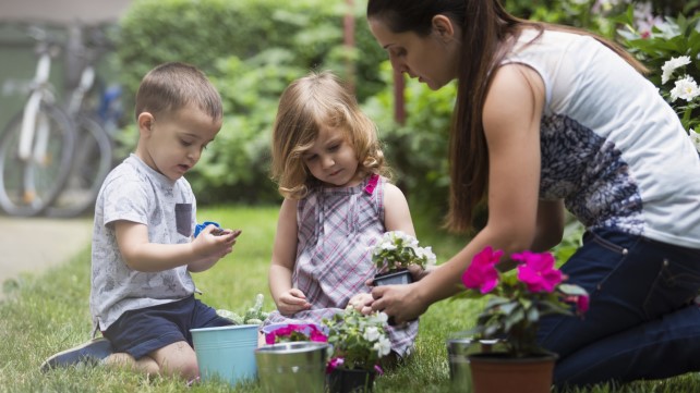 Mother with her children planting flowers in formal garden